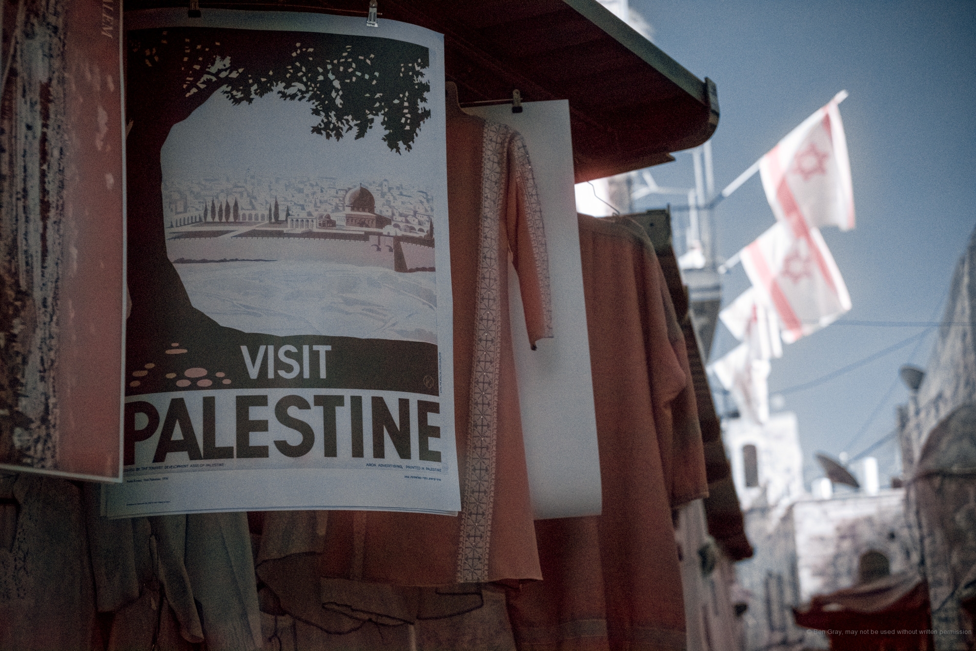A merchant's "Visit Palestine" poster hangs below the Israeli flags of a settler living in the Muslim quarter of Jerusalem's Old City.