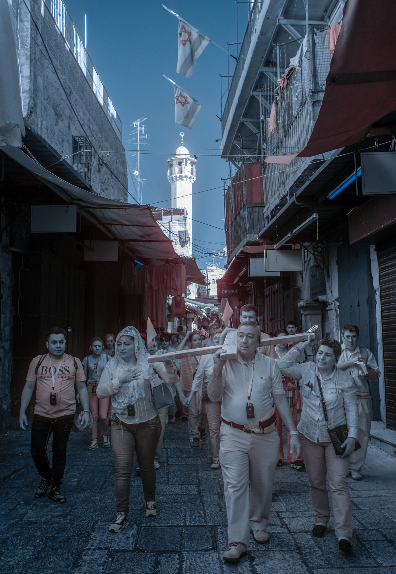 A group of Guatemalan pilgrims carry a cross along the Via Dolorosa under Israeli flags and the minaret of the mosque. The Via Dolorosa is the path Jesus was believed to have walked to his crucifixion.